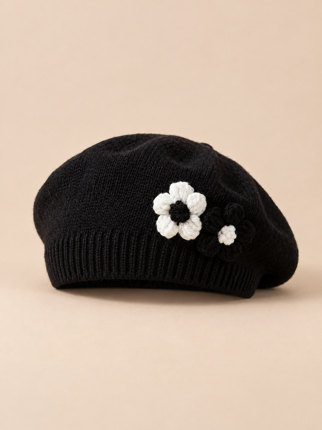 Béret bébé fille Noir à fleurs en relief au crochet, vue de face sur fond pêche sable