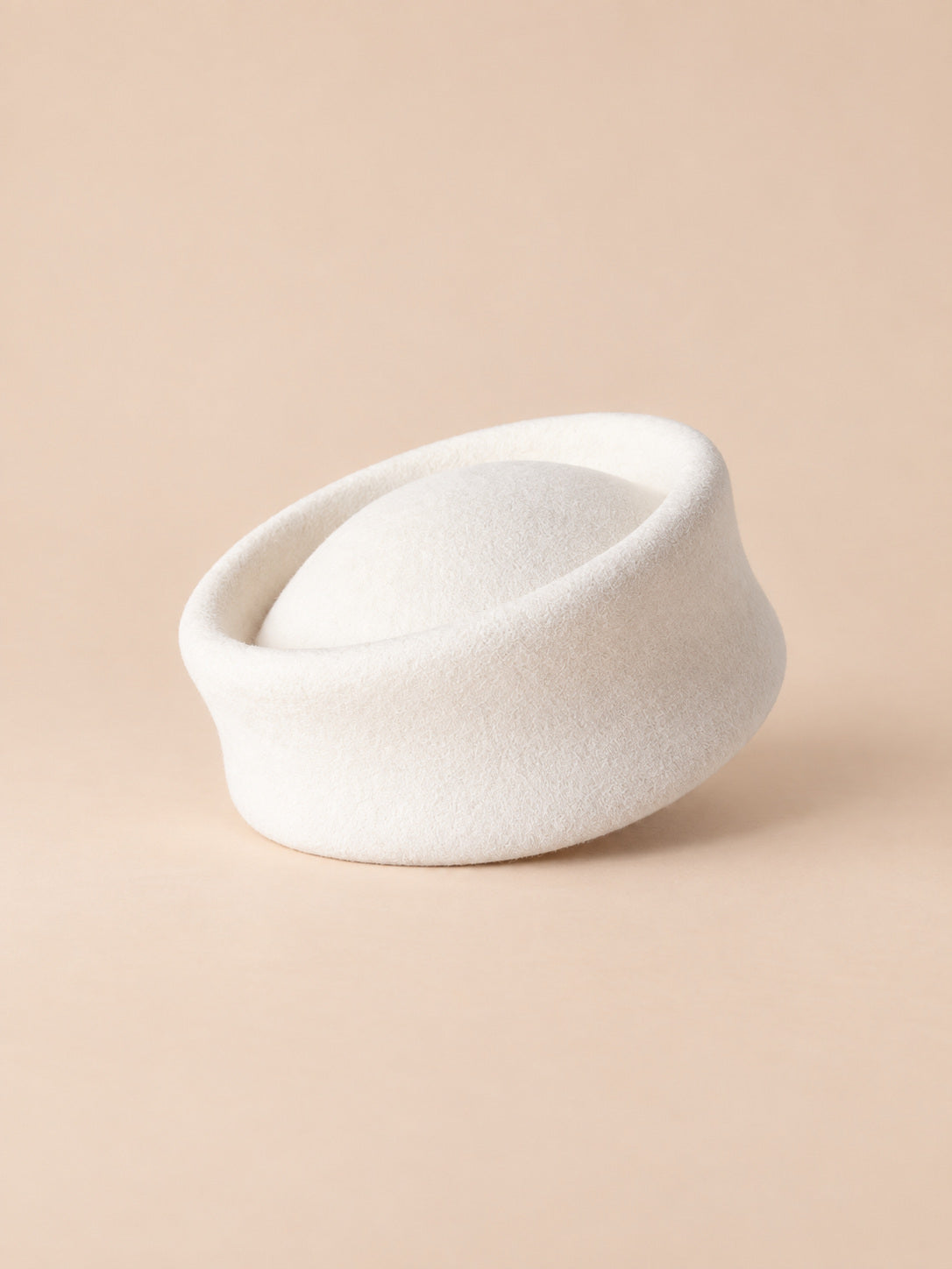 Béret femme en laine feutrée blanc, forme pork-pie, vue de face sur fond pêche sable