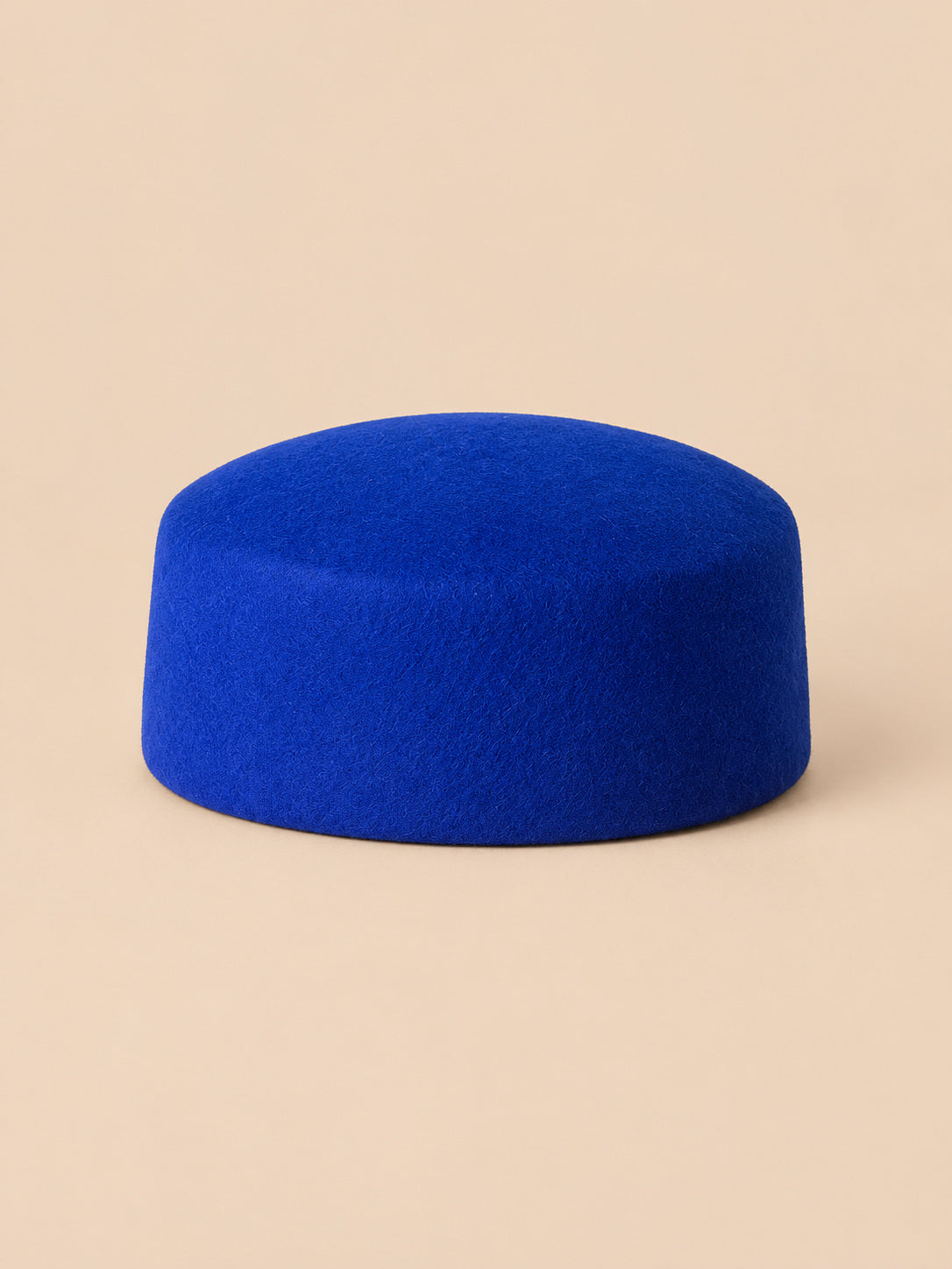 Béret femme en laine feutrée bleu, forme plat, vue de face sur fond pêche sable