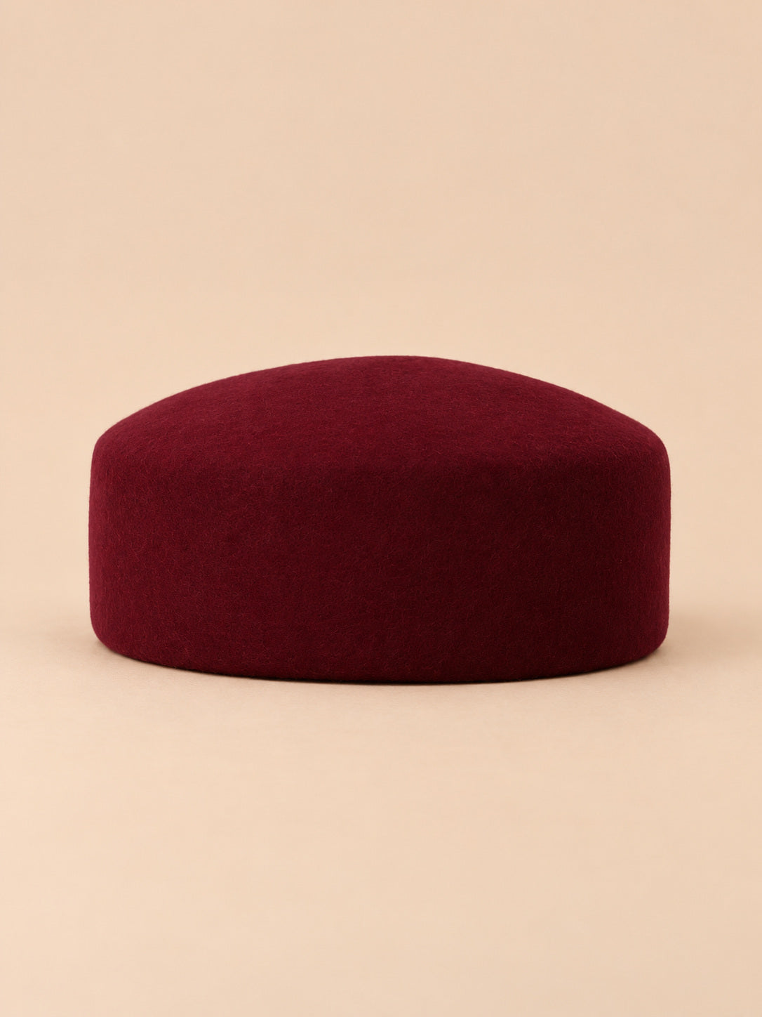 Béret femme en laine feutrée bordeaux, forme plat, vue de face sur fond pêche sable