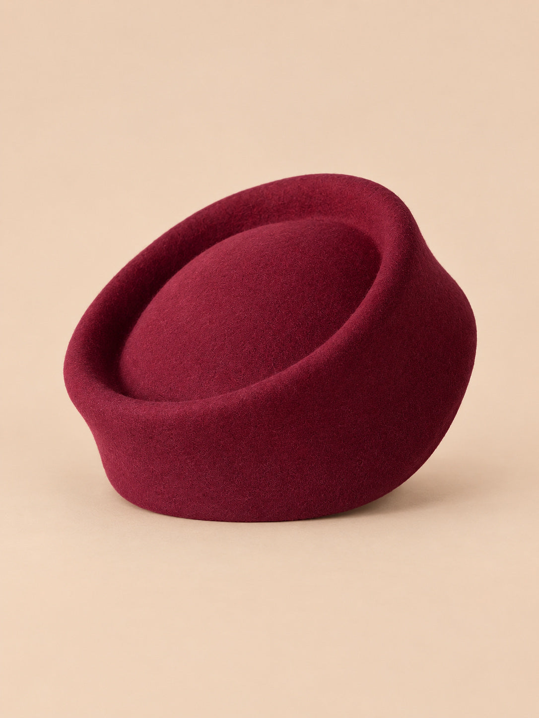 Béret femme en laine feutrée bordeaux, forme pork-pie, vue de face sur fond pêche sable