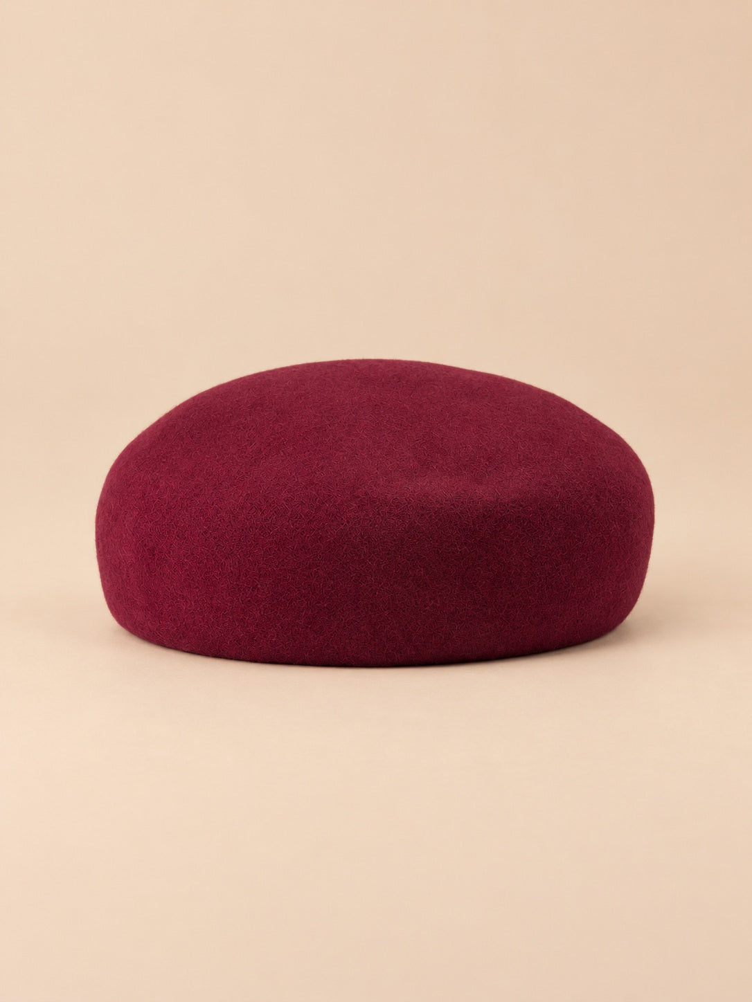 Béret femme en laine feutrée bordeaux, forme rond, vue de face sur fond pêche sable