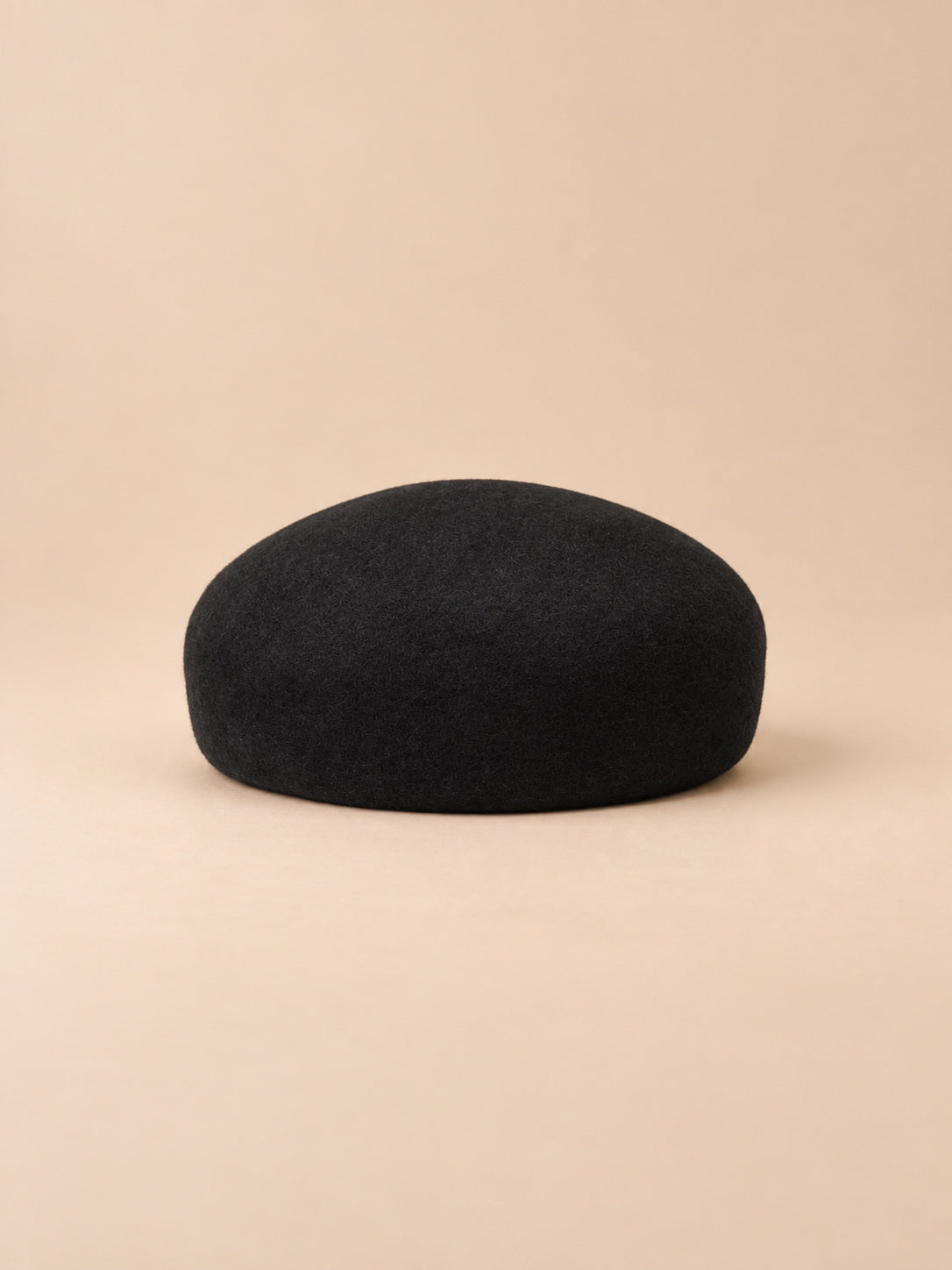 Béret femme en laine feutrée noir, forme rond, vue de face sur fond pêche sable