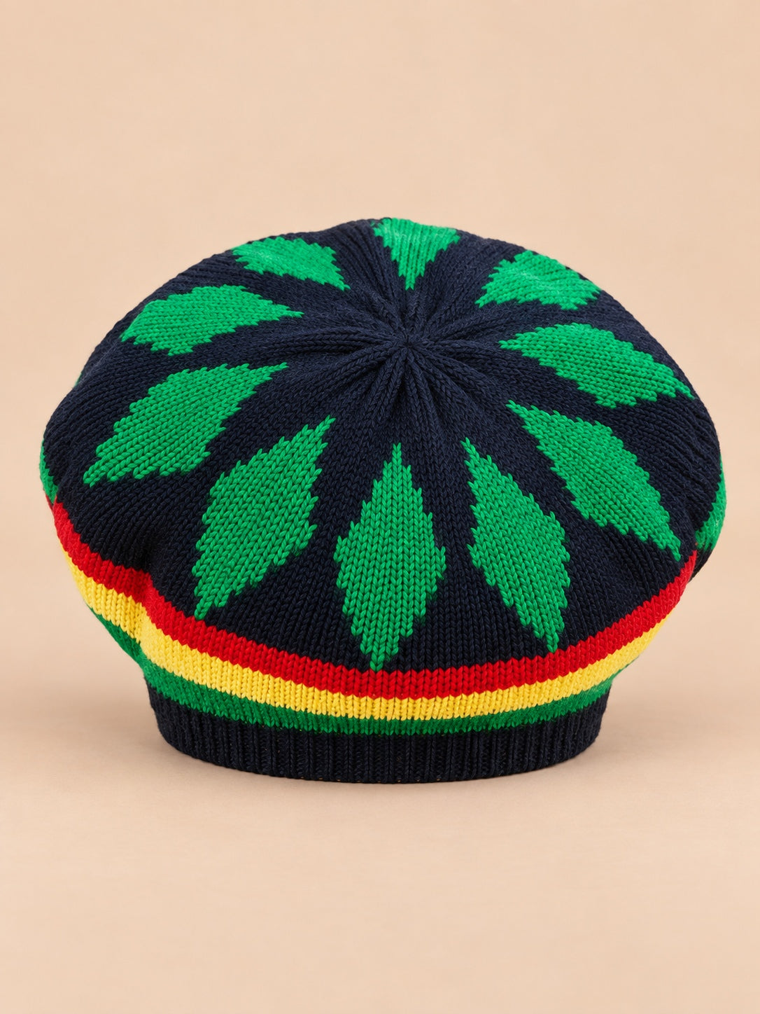 Béret rasta en maille multicolore 1, motifs verts sur fond sombre, vue de face sur fond sable pêche.