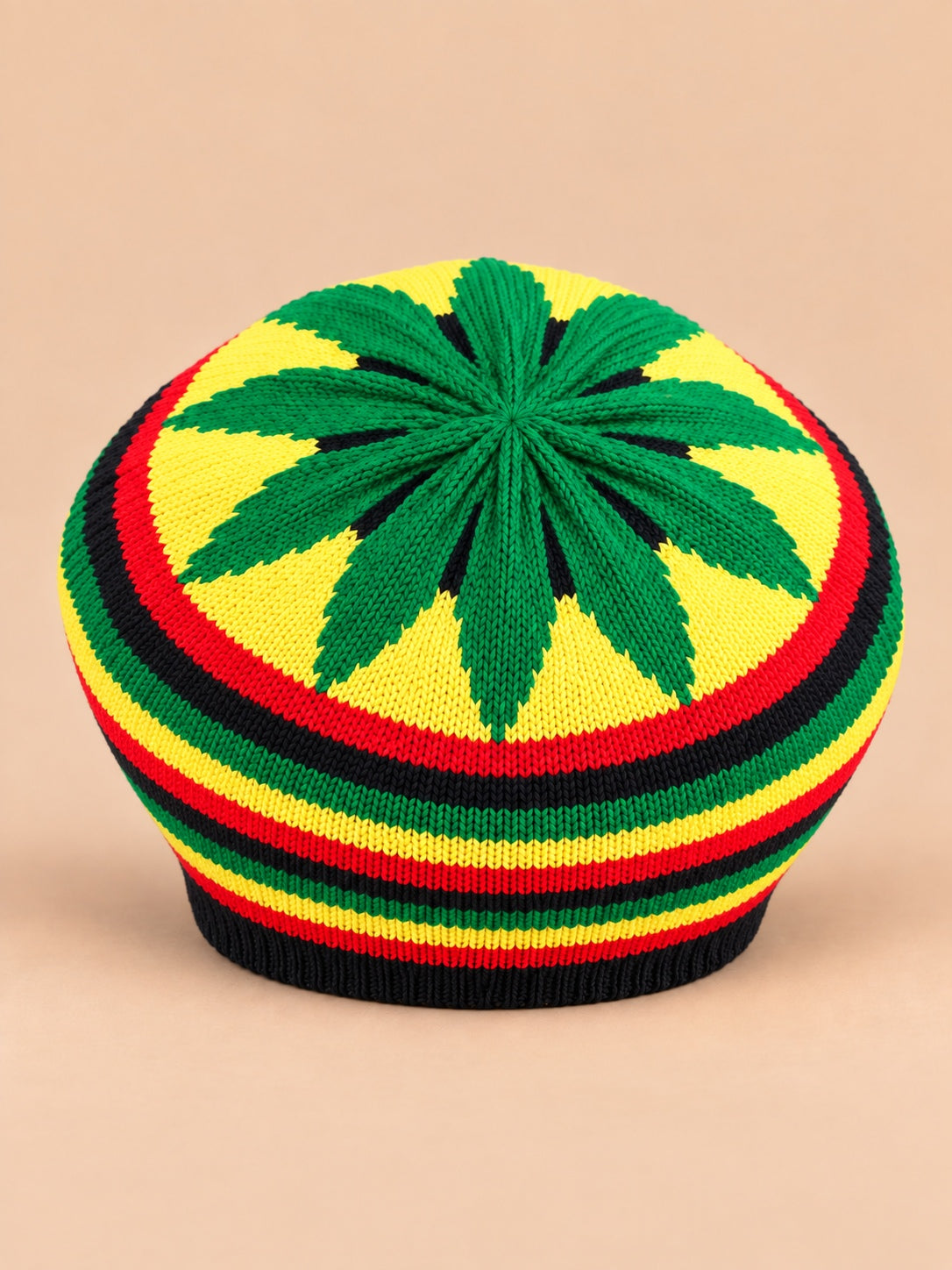 Béret rasta en maille multicolore 3, motifs verts et jaunes, vue de face sur fond sable pêche.