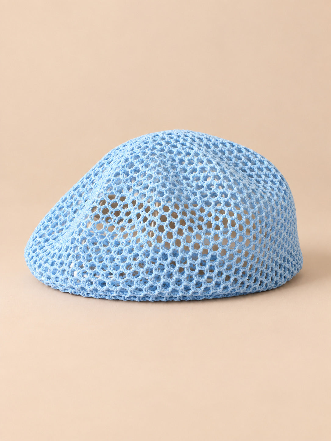 Béret résille ajouré bleu ciel, vue de face sur fond pêche sable