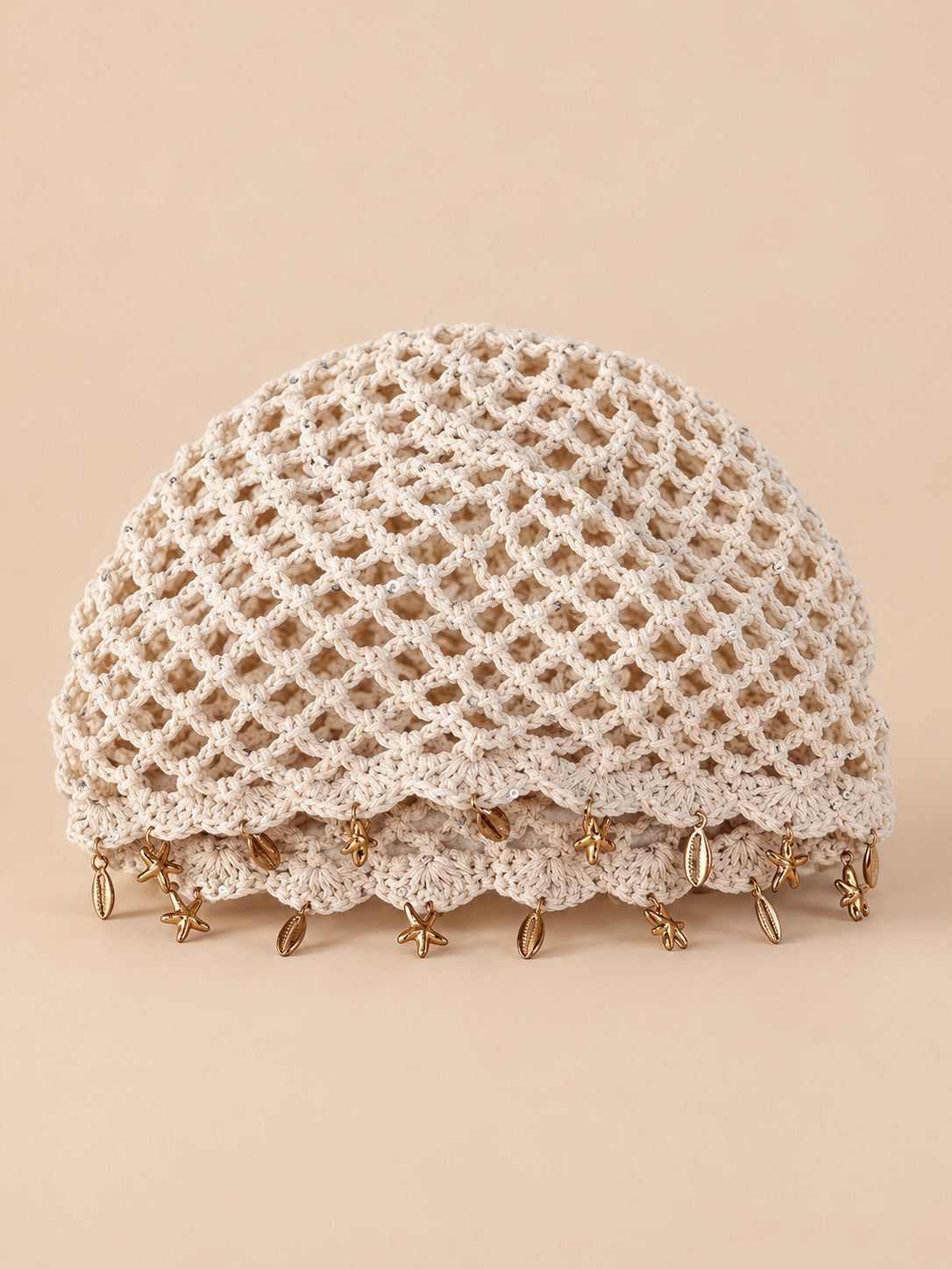 Béret rétro beige ajouré au crochet à franges d'étoiles dorées, vue de face sur fond pêche sable