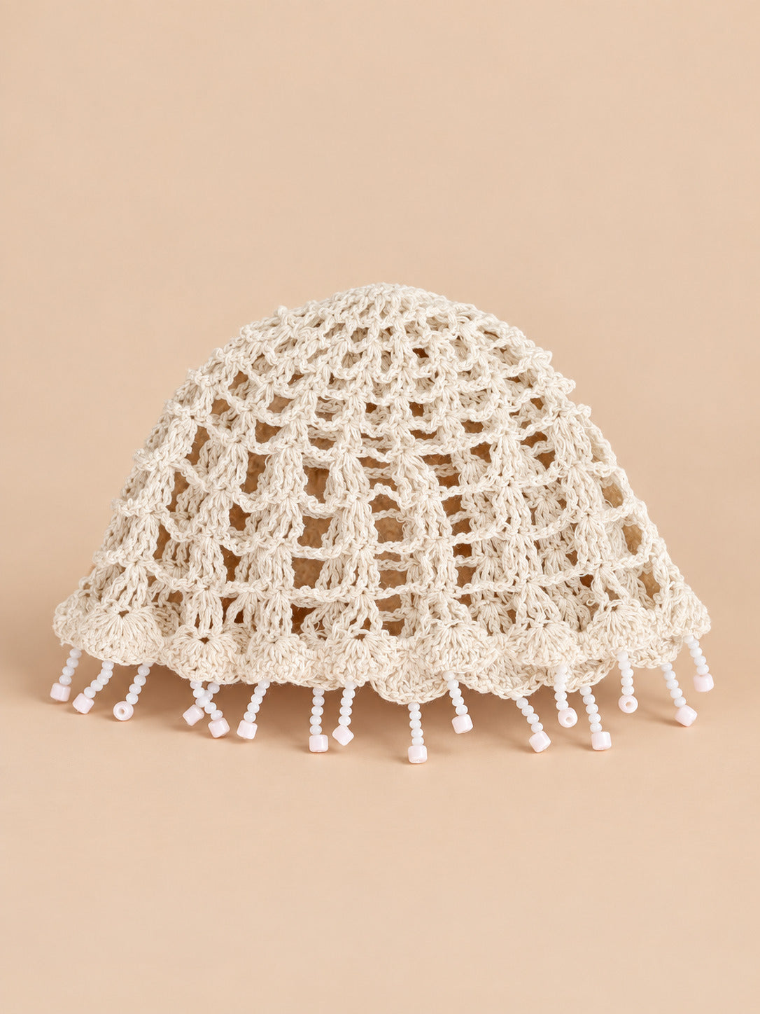 Béret crochet rétro blanc ajouré à franges de perles, vue de face sur fond pêche sable