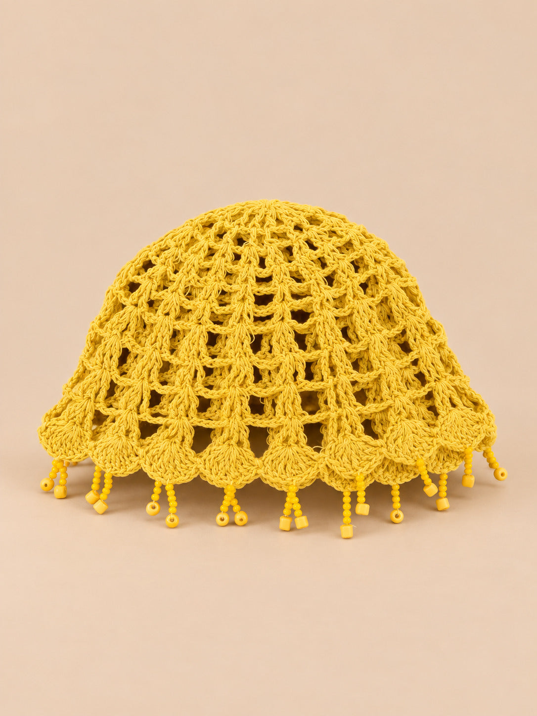 Béret crochet rétro jaune ajouré à franges de perles, vue de face sur fond pêche sable