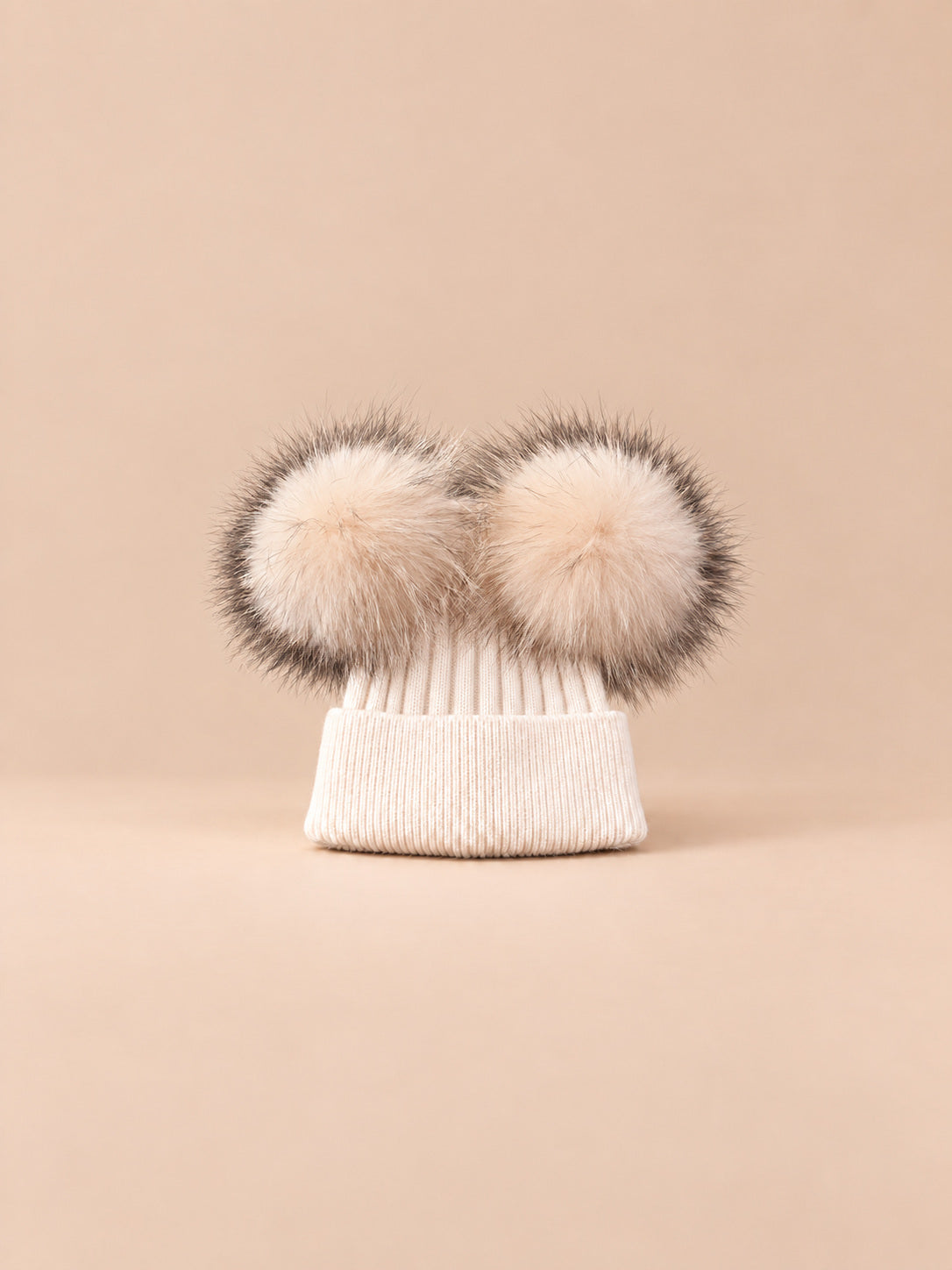 Bonnet double pompon, beige, pompons assortis, vue de face sur fond pêche sable.