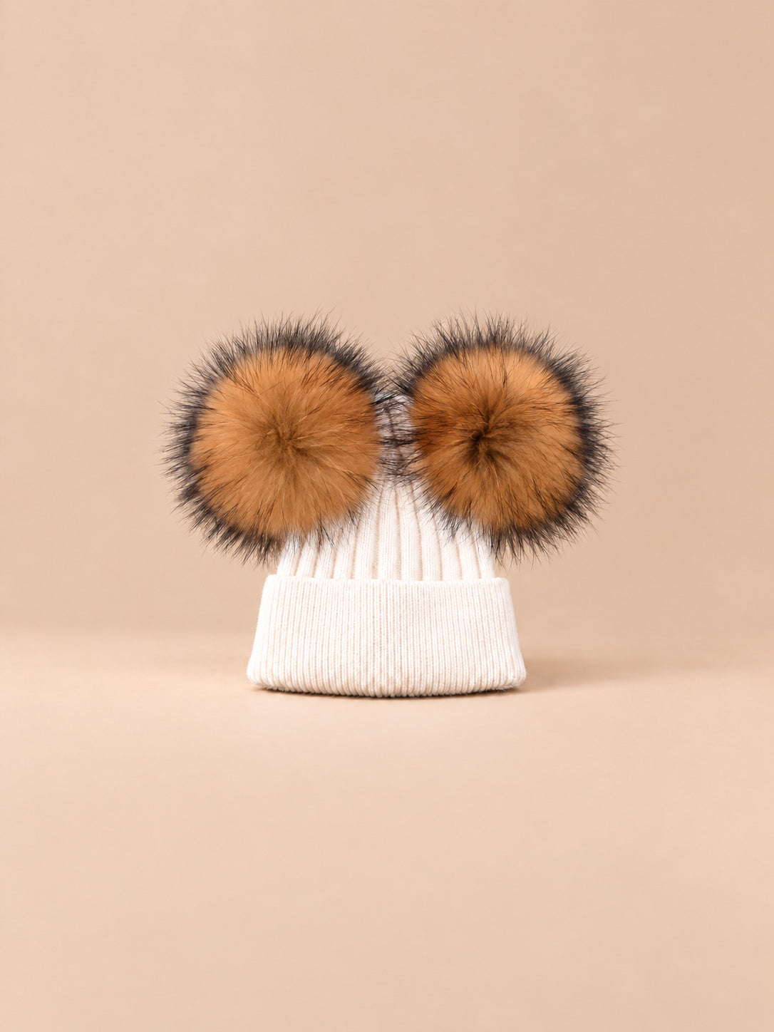 Bonnet double pompon, blanc, pompons naturels, vue de face sur fond pêche sable.