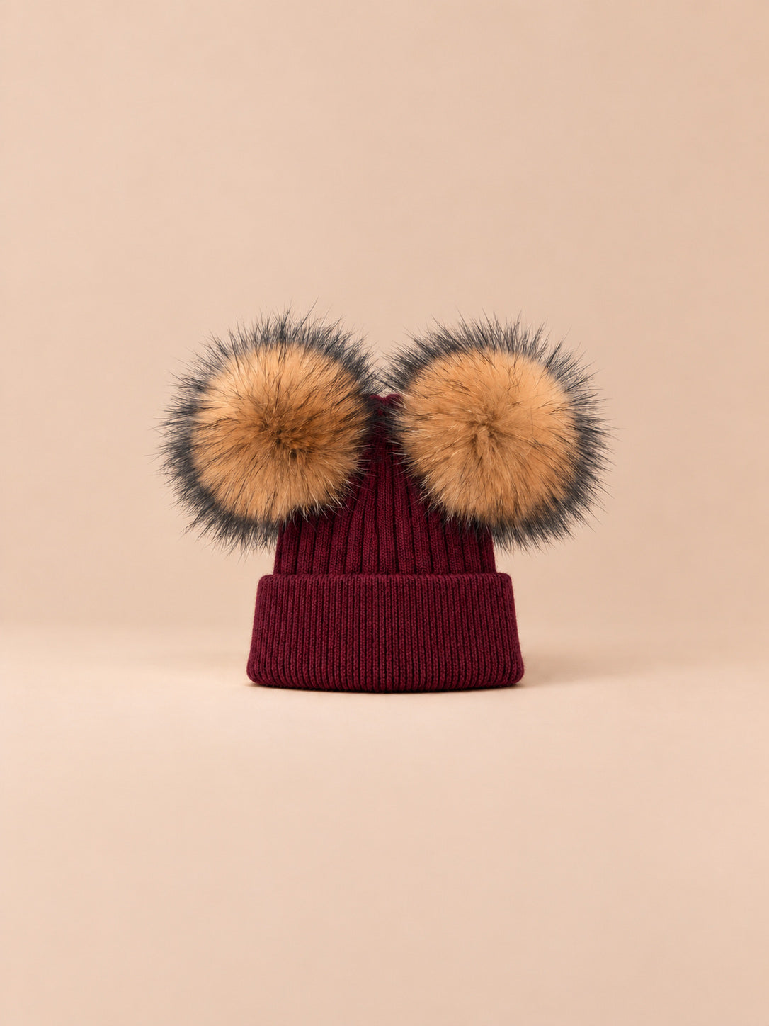 Bonnet double pompon, bordeaux, pompons naturels, vue de face sur fond pêche sable.