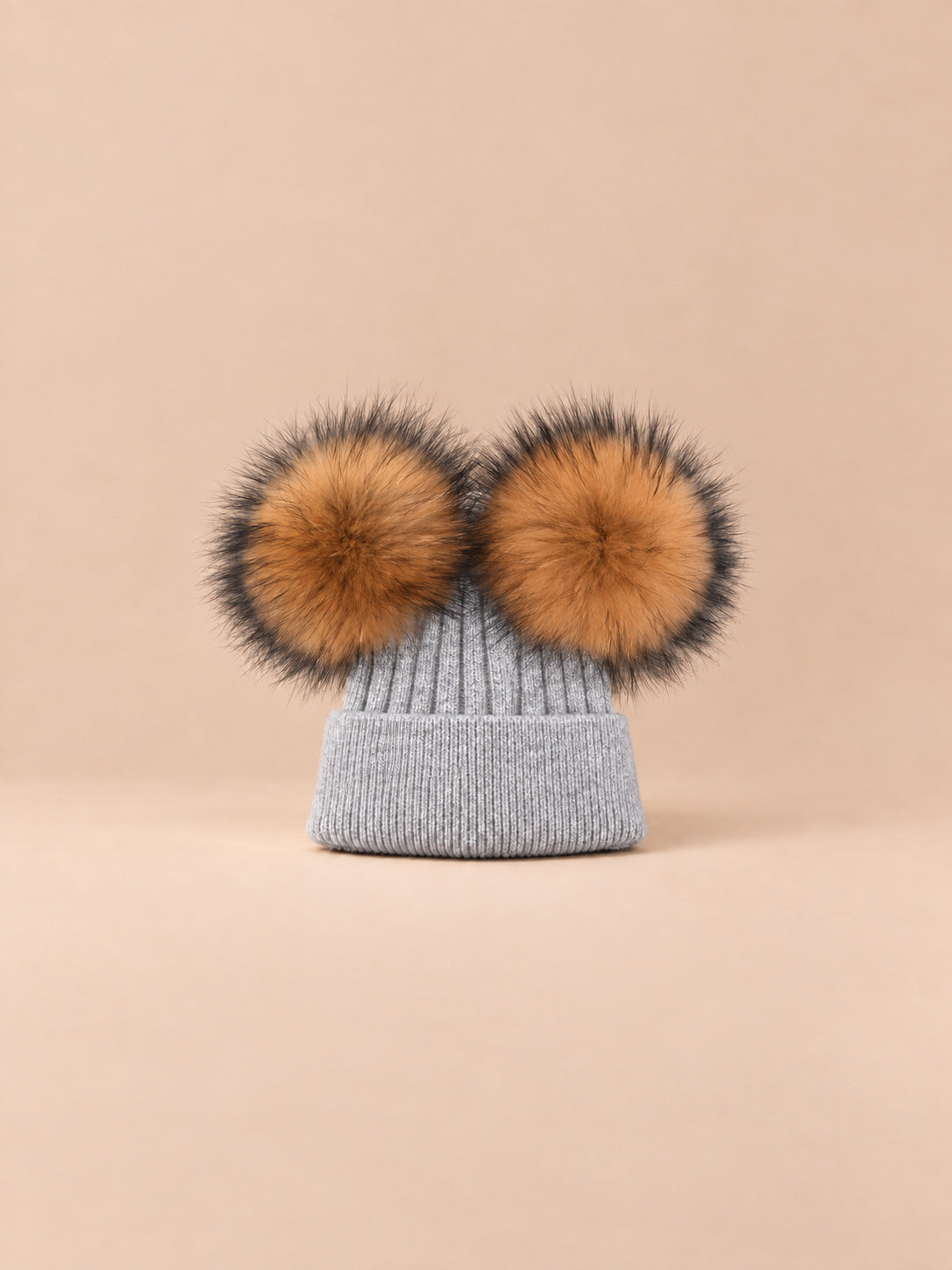 Bonnet double pompon, gris clair, pompons naturels, vue de face sur fond pêche sable.