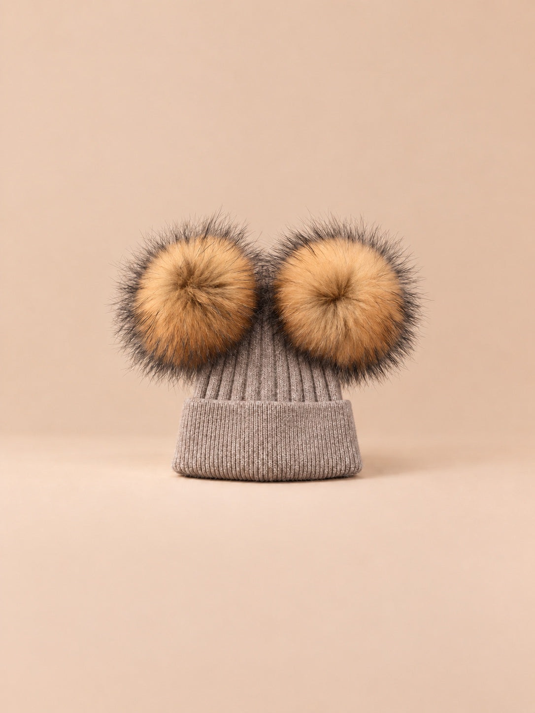 Bonnet double pompon, marron, pompons naturels, vue de face sur fond pêche sable.