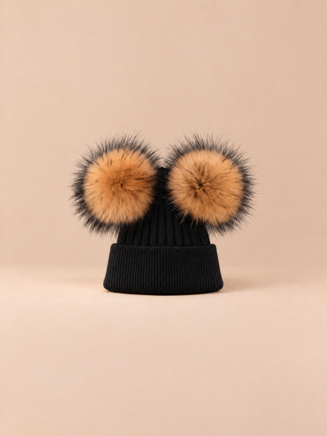 Bonnet double pompon, noir, pompons naturels, vue de face sur fond pêche sable.