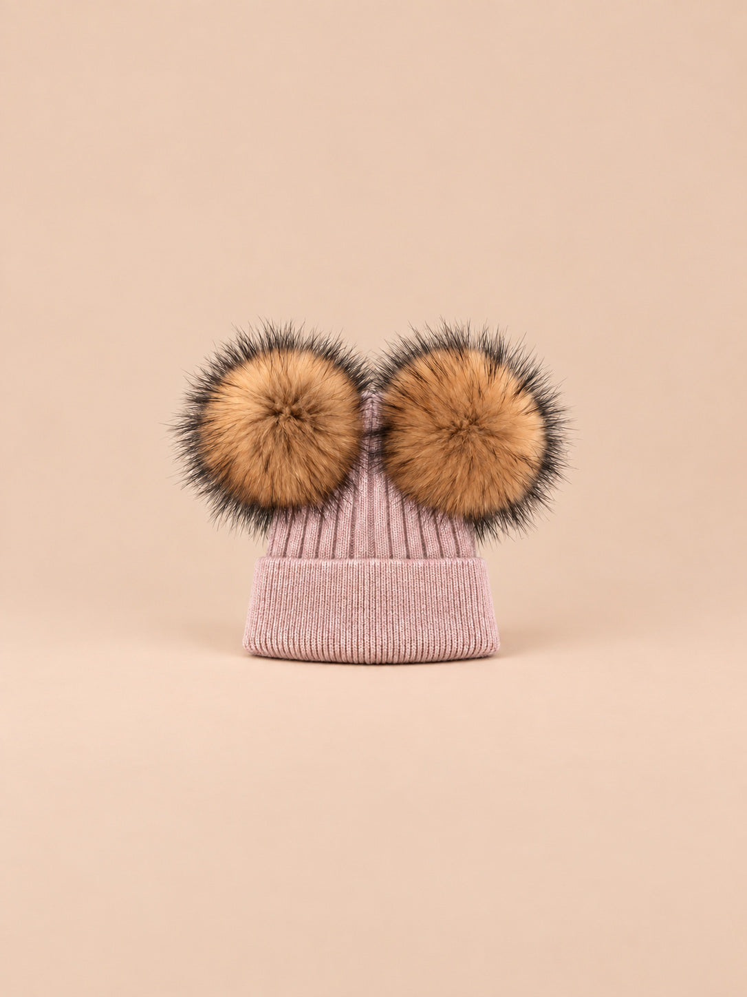 Bonnet double pompon, rose poudré, pompons naturels, vue de face sur fond pêche sable.