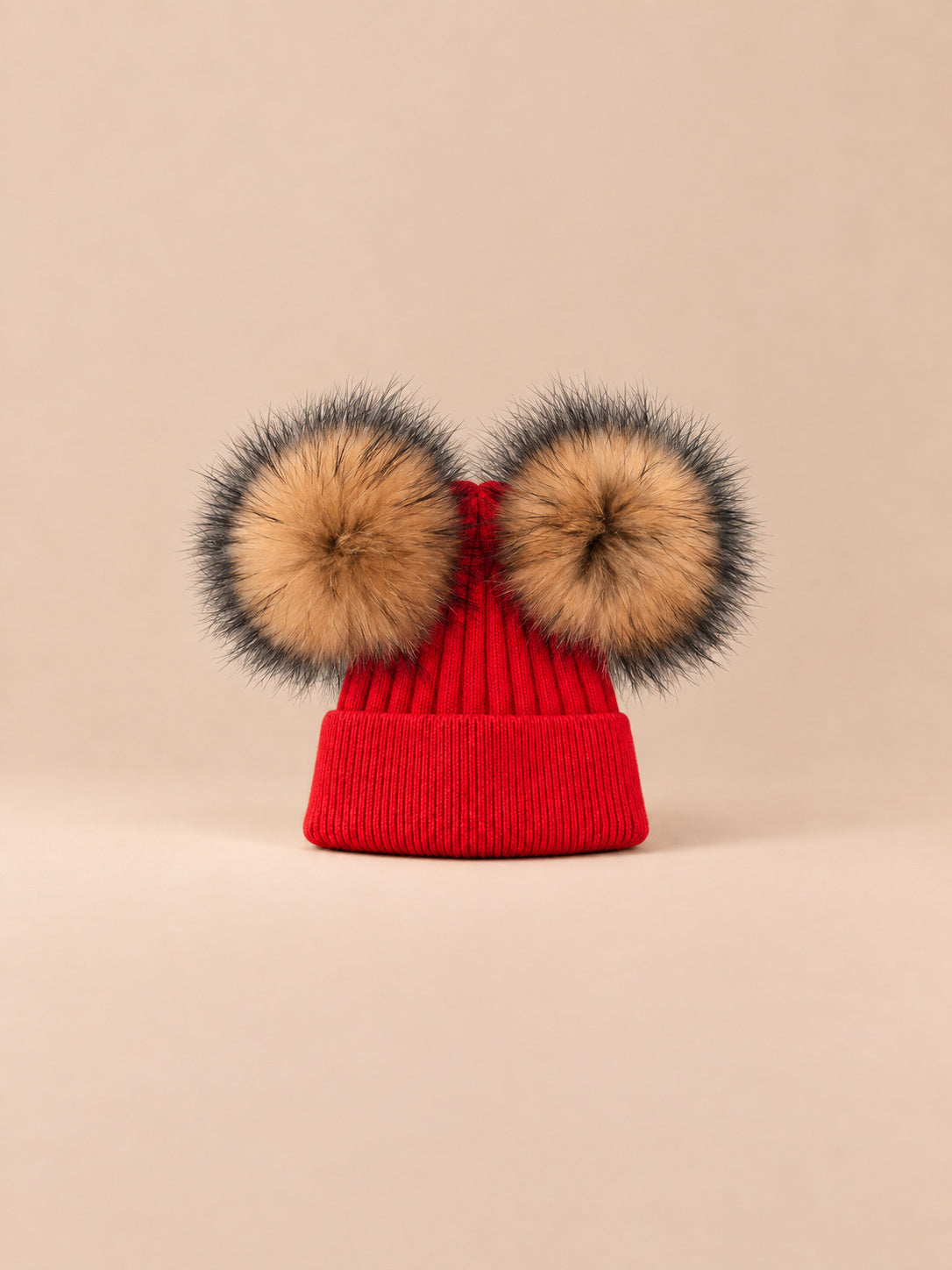 Bonnet double pompon, rouge, pompons naturels, vue de face sur fond pêche sable.