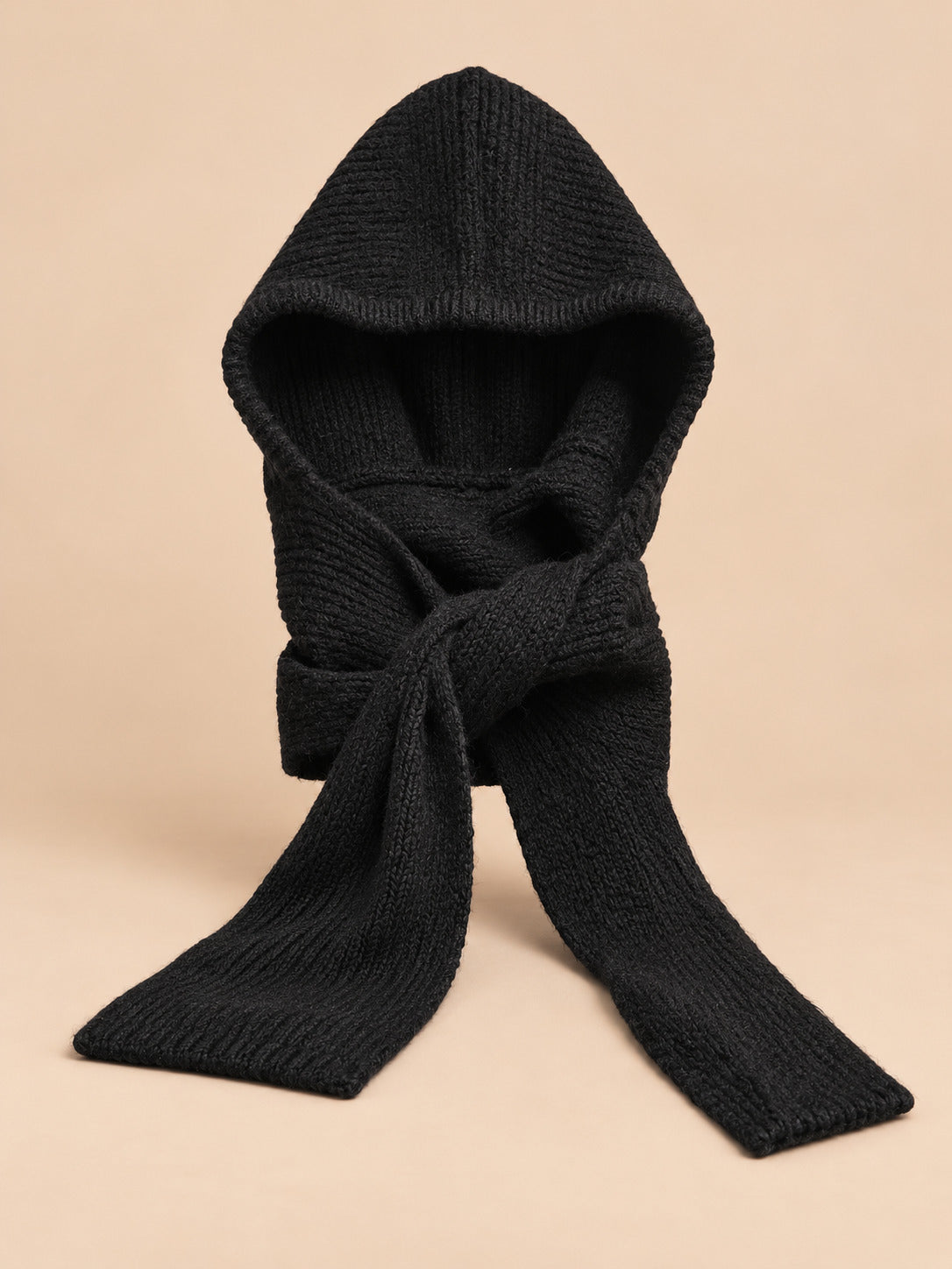 Cagoule bonnet-écharpe noir en maille, vue de face sur fond pêche sable