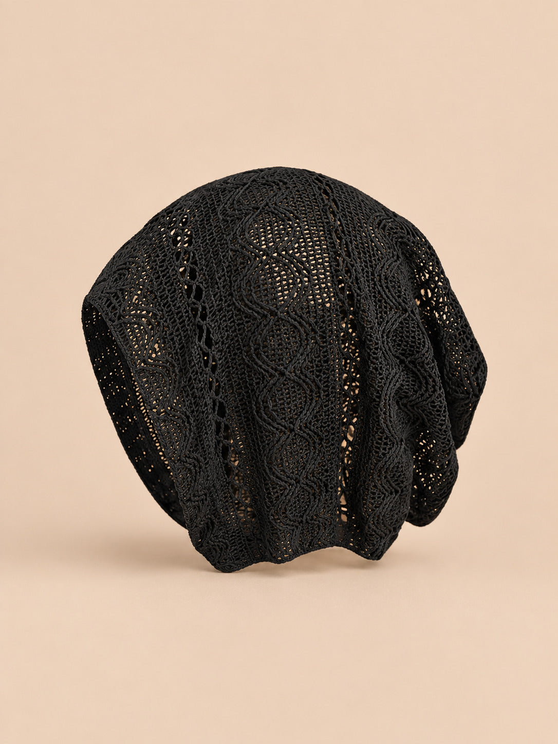 Bonnet calotte froncée noir en dentelle crochet ajourée, vue de face sur fond pêche sable