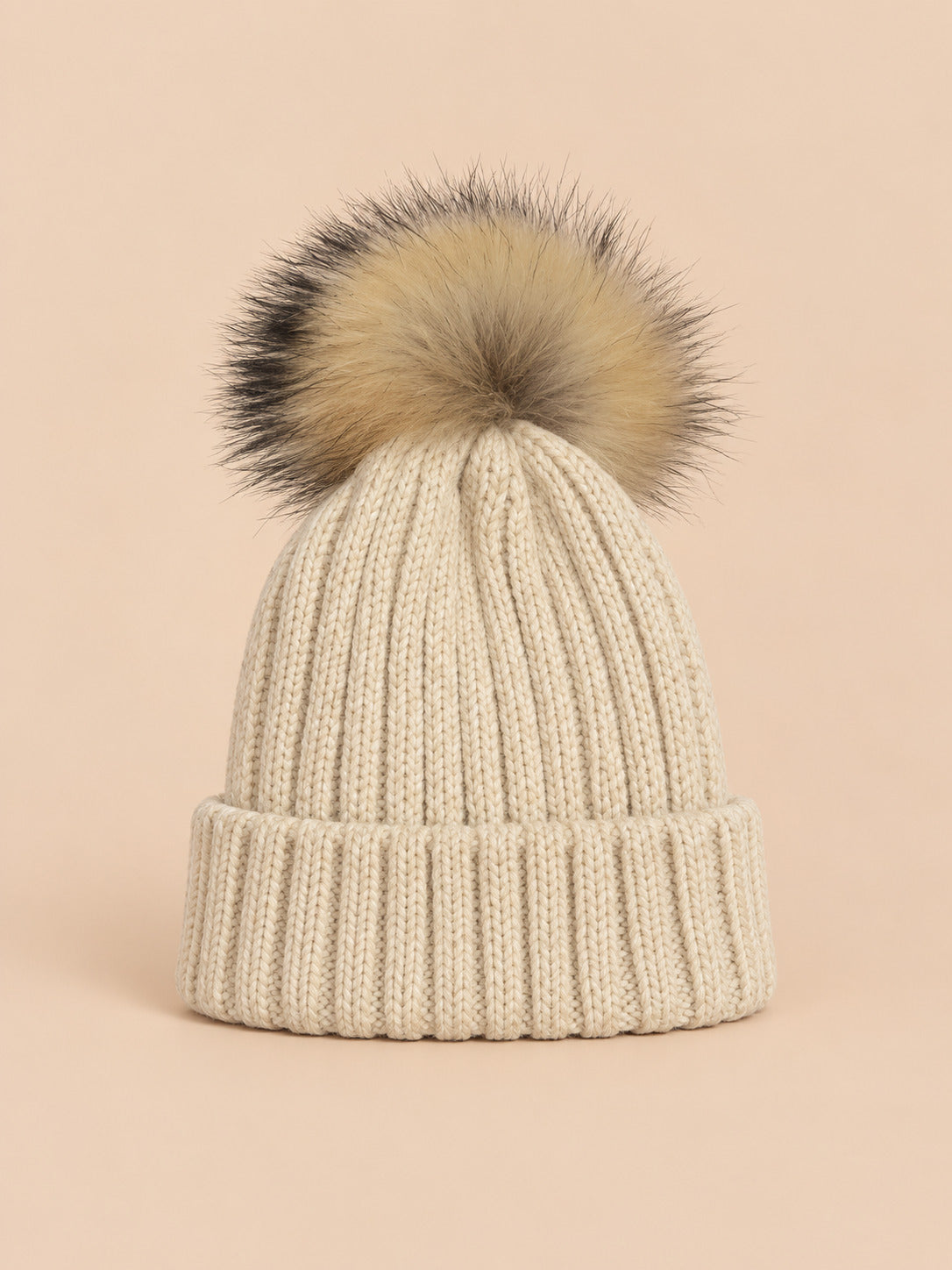 Bonnet enfant à pompon beige, vue de face sur fond pêche sable