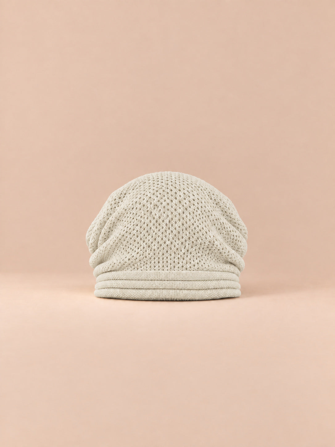 Bonnet oversize en maille beige, vue de face sur fond pêche sable.