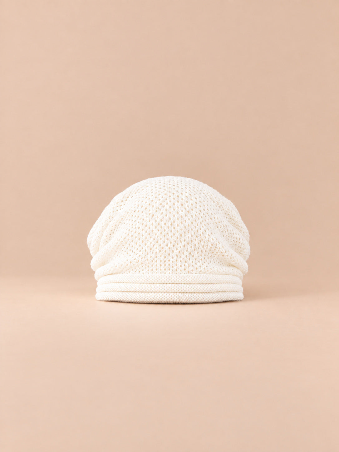 Bonnet oversize en maille blanc, vue de face sur fond pêche sable.