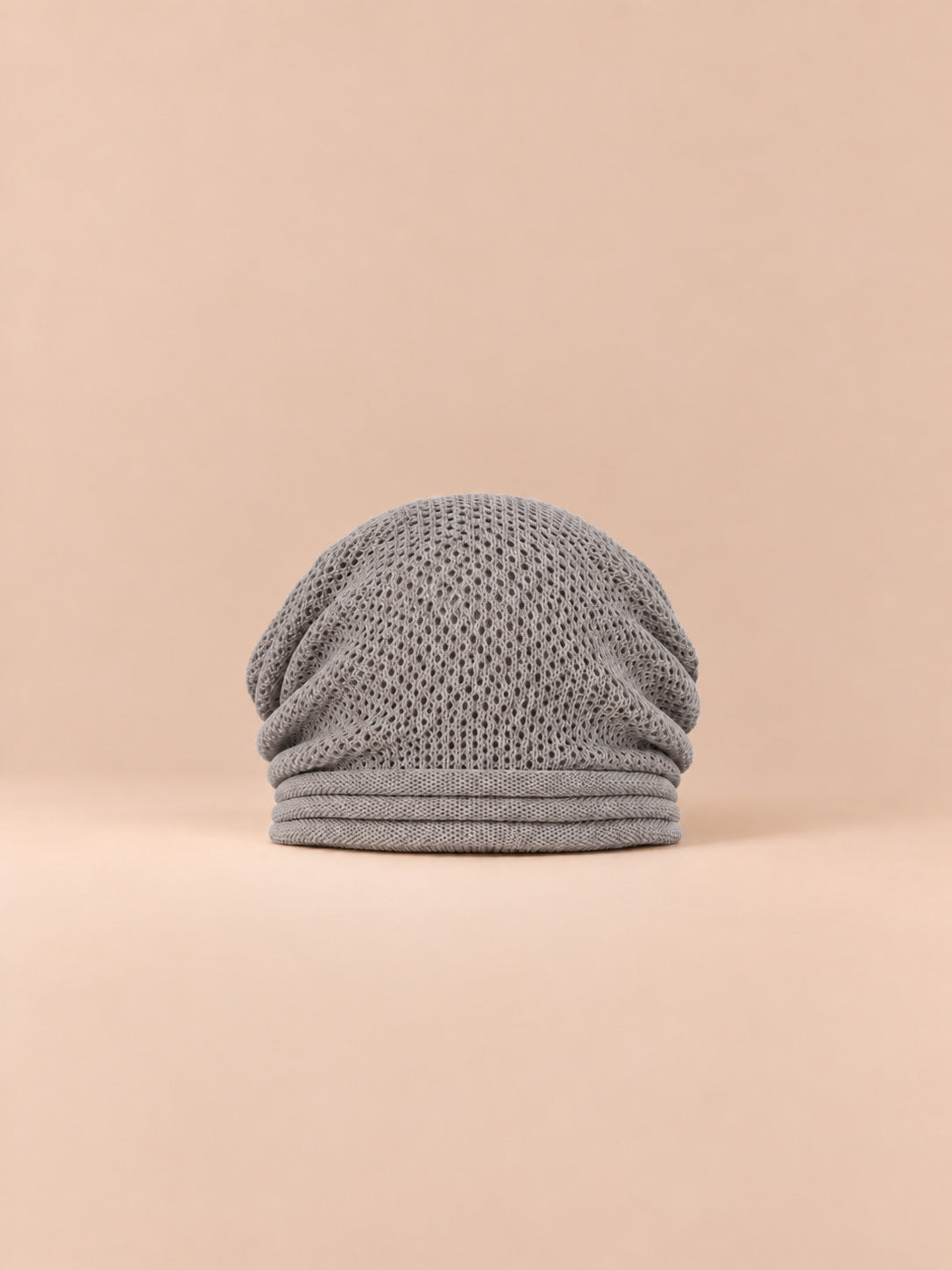 Bonnet oversize en maille gris clair, vue de face sur fond pêche sable.