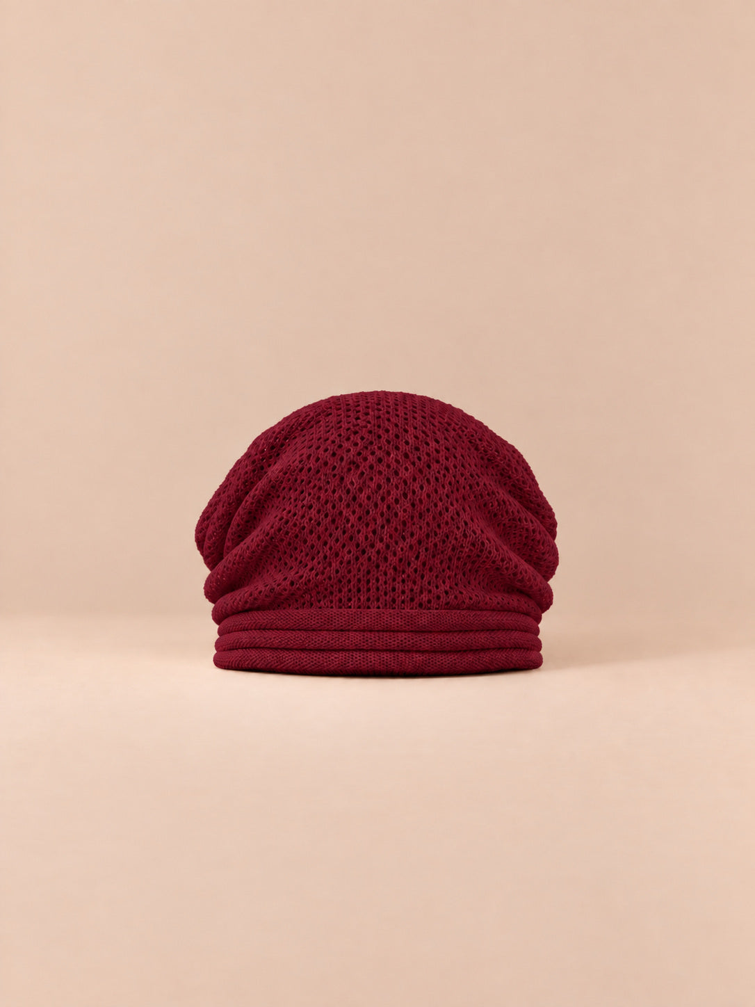 Bonnet oversize en maille rouge, vue de face sur fond pêche sable.