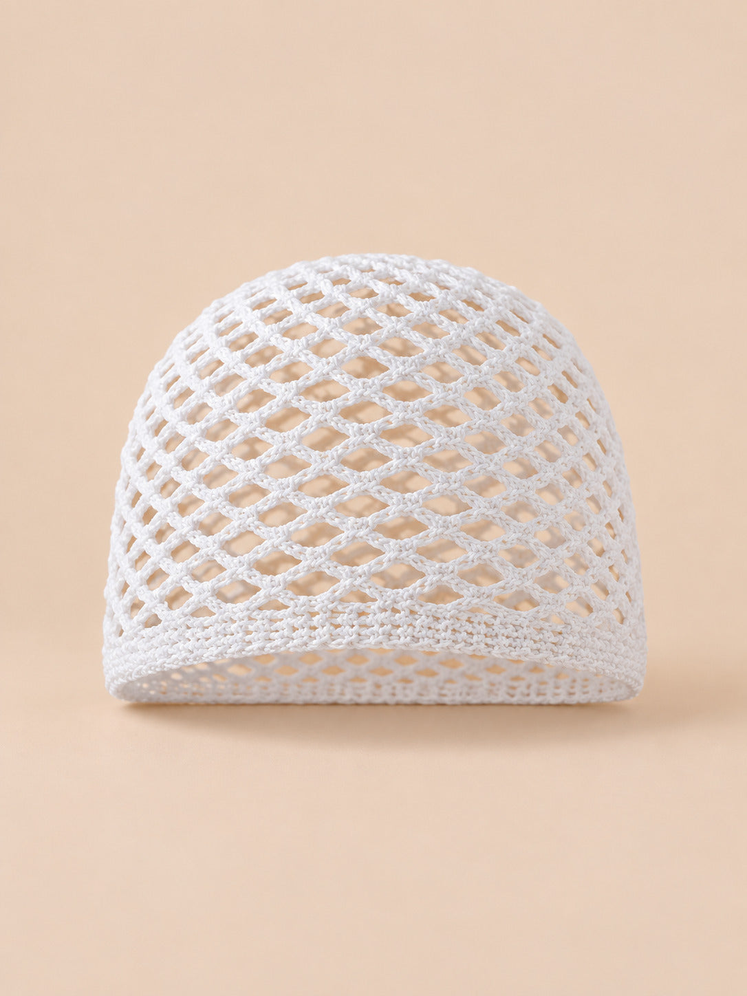 Bonnet fin femme blanc en coton résille ajouré, vue de face sur fond pêche sable