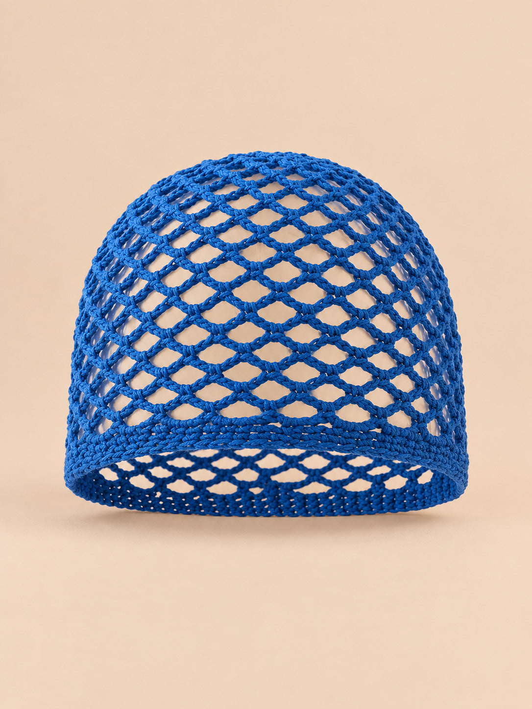 Bonnet fin femme bleu roi en coton résille ajouré, vue de face sur fond pêche sable
