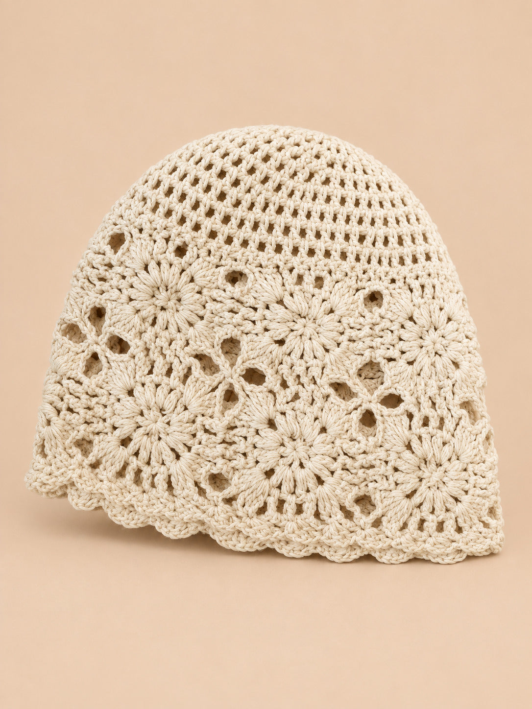 Bonnet turban femme beige ajouré à fleurs au crochet, vue de face sur fond pêche sable
